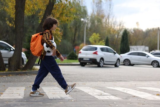 Little boy with backpack and ball walking on pedestrian crossing outdoors, space for text. Child in danger and road safety - Powered by Adobe