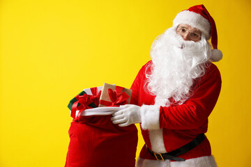 Santa Claus with bag full of gifts on yellow background, space for text. Merry Christmas and Happy New Year
