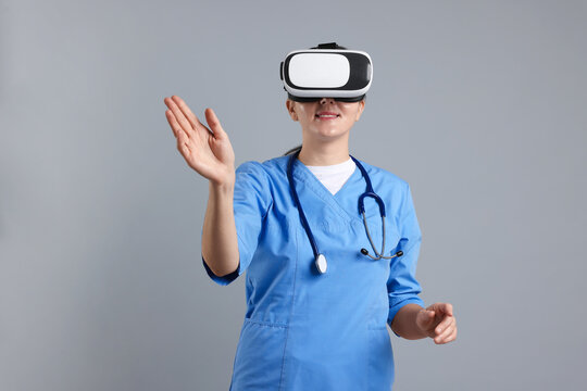 Modern technology. Doctor in headset using virtual screen on grey background - Powered by Adobe