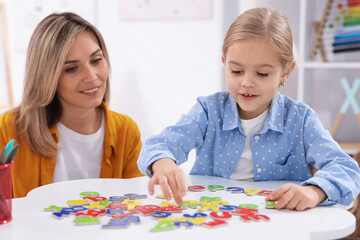 Fototapeta premium Mother teaching her daughter alphabet at white table indoors