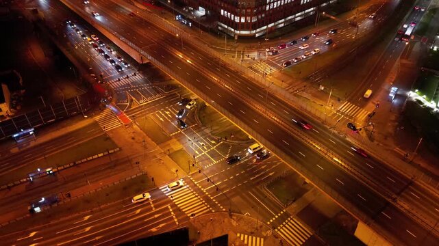 Aerial time lapse of vibrant city intersection at night with dynamic traffic flow. Urban evening landscape. Lifestyle and rhythm of modern city. Convenient interchange for cars and public transport