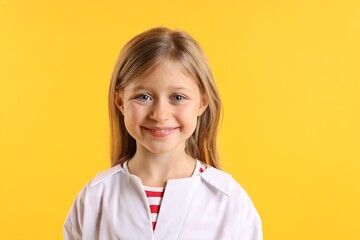 Portrait of smiling little girl in laboratory coat on yellow background. Child and science