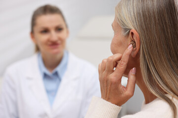 Obraz premium Senior woman with hearing aid having appointment with doctor in clinic, selective focus