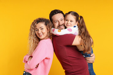 Happy family hugging and posing on yellow background