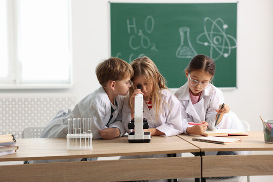 Group of children with microscope studying at desk in class. Little scientists