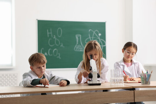 Group of children with microscope studying at desk in class. Little scientists