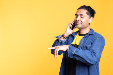 Confident joyous indian guy calling people on telephone line, laughing and discussing with friends on a phone call against orange background. Young adult being upbeat and friendly.