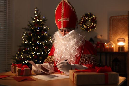Saint Nicholas reading letter at desk in room decorated for Christmas