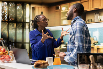 Upset African American couple fighting at home in their kitchen. Black woman looks offended and...