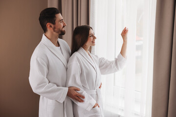 Happy couple wearing bathrobes near window in hotel room