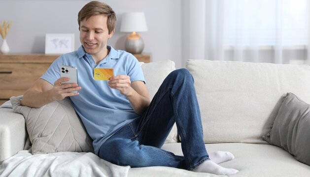 Young man making online payment with phone and credit card indoors, space for text