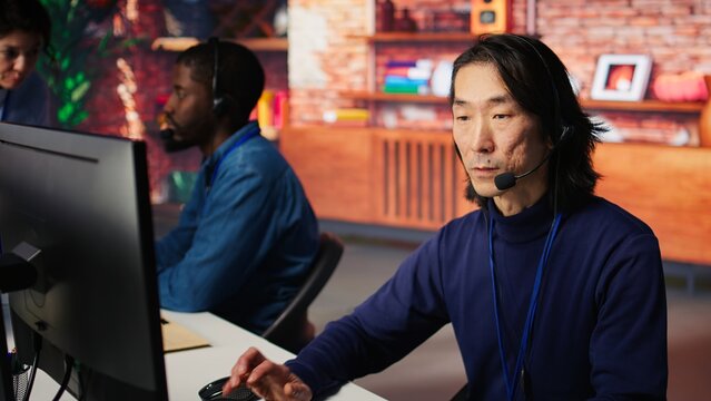 Joyous technical support senior agent in call center office doing troubleshooting. Jolly experienced Asian IT worker fixing customer connectivity issues using computer, camera B - Powered by Adobe