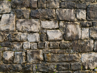 A wall made of stone with moss growing on it. The wall is gray and brown in color. Background for design, Stone mason craft.
