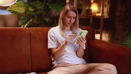 white woman on sofa frowning while checking phone and attempting to fix app issue with coffee nearby in warm