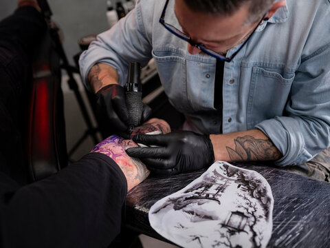 Tattoo artist working on Japanese landscape sleeve with reference stencil visible on workspace table in studio. - Powered by Adobe