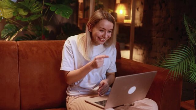 Smiling young blond woman looking at laptop and have a video call conference meeting with family or friends at home alone. Happy blond female has pleasant conversation. 