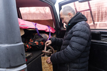 A middle-aged man with short hair is sitting in a car, focused on repairing a vehicle. There's a dog in the passenger seat.