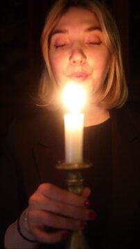 Vertical video of a young woman blowing out a candle while looking into the camera in a dim historic room, holding a 16th-century candlestick. Symbol of closure, reflection, and the end of a day or ce
