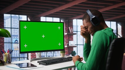Black employee in his loft using green screen PC to analyze sales reports and plan business growth, remote job. Young man working from home doing project research, typing on computer. Camera B.