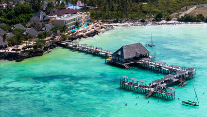 Aerial view of a tropical resort with overwater bungalows, turquoise sea, and palm trees.