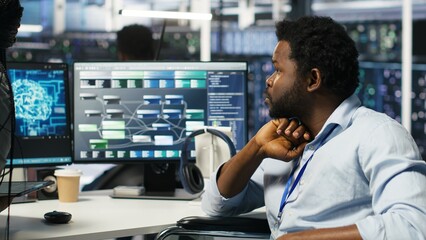 Data center engineer in wheelchair and colleague oversee automated tasks using node tree programming tool. Inclusive server farm team adjusts system settings based on AI analytics, camera B