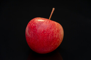 A ripe red apple stands on a smooth black surface under studio lighting.