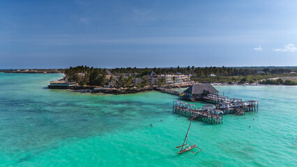 Tropical island resort with overwater restaurant, bungalows, and clear turquoise ocean.