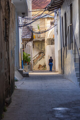 Person walks down a narrow, old alleyway with historic buildings and overhead wires.
