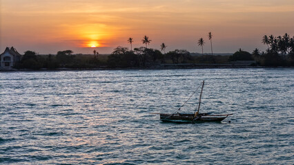 Sunset over tropical waters with a traditional boat and palm-lined coast.