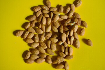 Raw shelled almonds scattered on yellow background