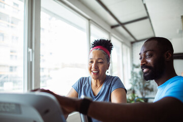 Senior woman with adult trainer exercising at gym, smiling