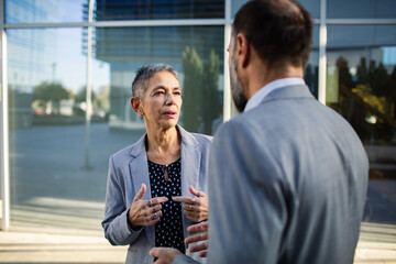 Senior woman and adult man having serious discussion outside office