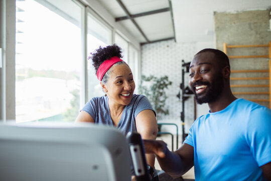 Mature woman and adult man smiling on cardio machine at gym
