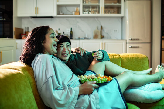 Adult lesbian couple laughing and cuddling on sofa at home