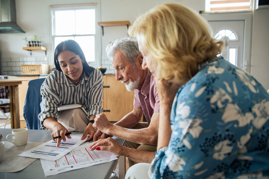 Young advisor helping senior couple with finances at home, focused
