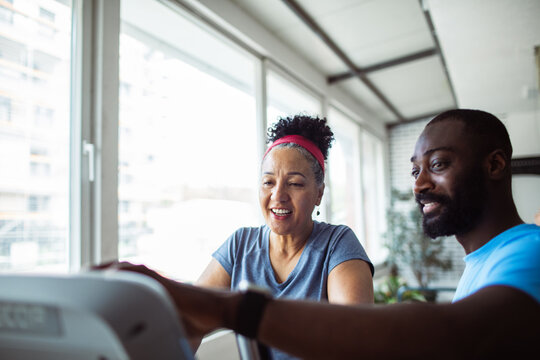 Senior woman with adult trainer exercising at gym, smiling