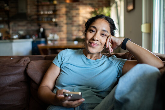 Young woman relaxing with smartphone at home, content