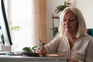 Mature woman writing notes at home desk
