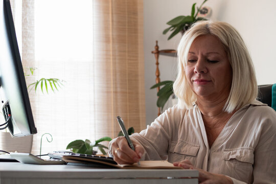 Mature woman writing notes at home desk