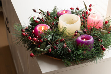 advent wreath with candles lit on a white sideboard in dining room