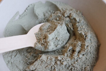 Close-up of a bowl of green clay with a wooden spoon. A wooden spoon with gren clay. Healing with green clay. Skin mask with green clay.