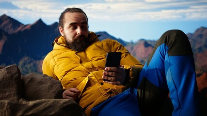 Traveler in warm clothing scrolling social media on top of the mountain peak, person always...