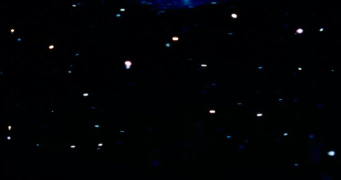 Red, blue, and silver particles drift through water in a dark space, reflecting cool and warm light&mdash;cosmic, dreamy, glittering star-like movement.
