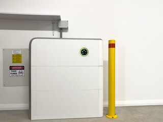 Horizontal shot Solar electric battery storage unit in a garage  on white wall safety post and warning sign