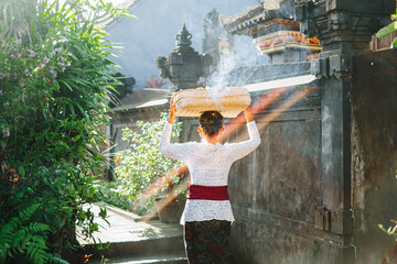 Woman carrying offering with smoke in front of Balinese temple