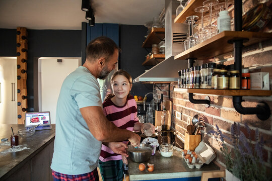 Adult father and child daughter baking together in home kitchen, smiling