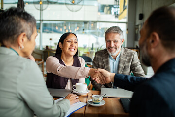 Adult colleagues smiling as they shake hands in cafe