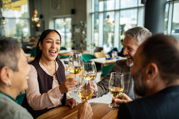 Adult and mature friends laughing and toasting with wine at restaurant