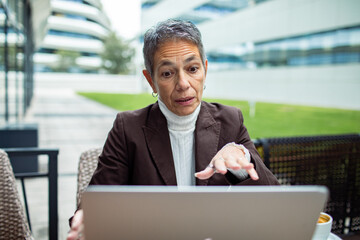 Mature businesswoman looking concerned on laptop in office courtyard