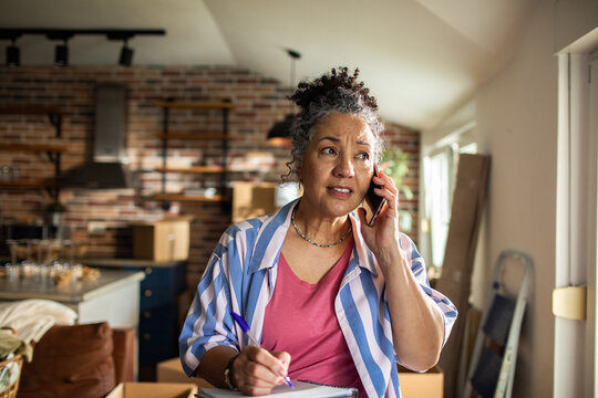 Mature woman concerned on phone while organizing boxes at home - Powered by Adobe
